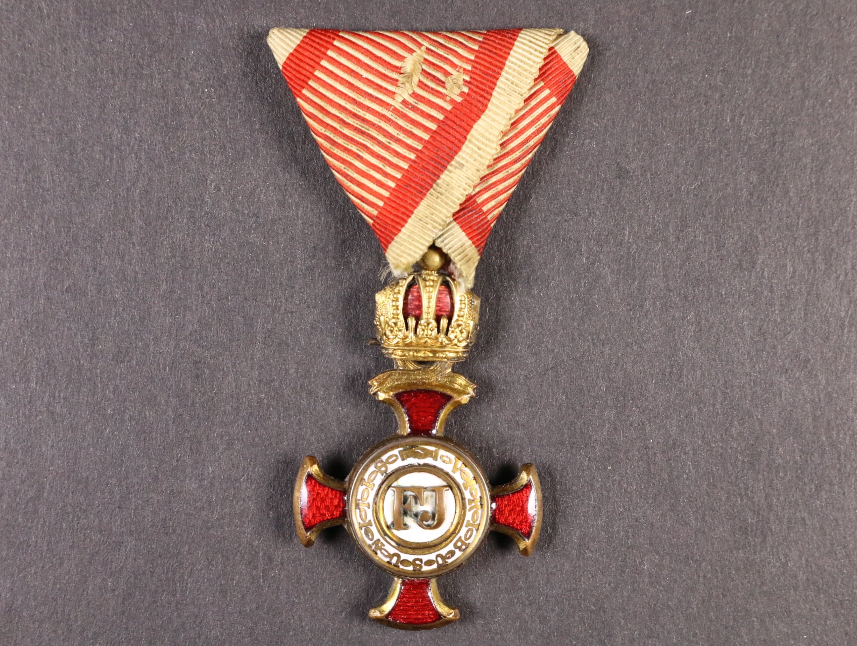 Zlatý záslužný kříž s korunou, na závěsném kroužku hvězdička a značka výrobce Wilh. Kunz Wiwn, pozlacený bronz, na spodním rameni na reversu vypadený smalt